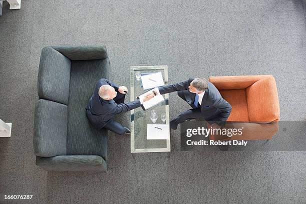 businessmen shaking hands across coffee table in lobby - face to face interview stock pictures, royalty-free photos & images