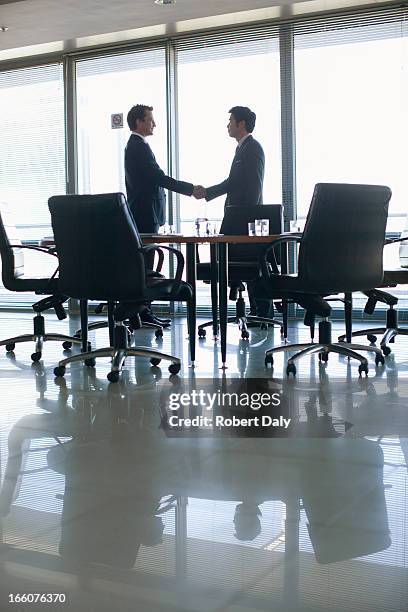 silhouette of businessmen shaking hands in conference room - handshake silhouette stock pictures, royalty-free photos & images