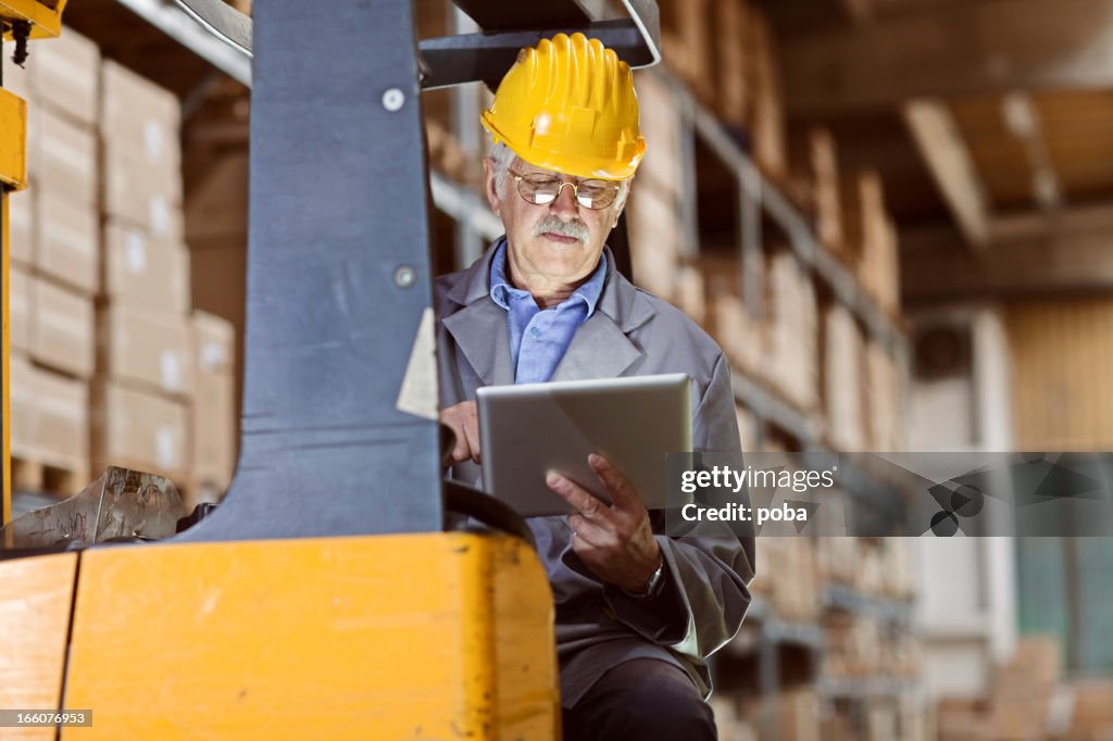 Operador de máquina elevadora em armazém usar tablet digital para rever o inventário