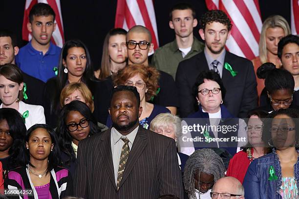 Wearing green ribbons in solidarity with the families of the Sandy Hook shooting victims, audience members listen as U.S. President Barack Obama...