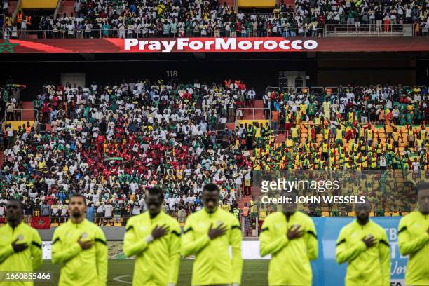 Supporters look on as the Senegalese football team sing their national anthem as "Pray for Morocco" is shown in the background ahead of the friendly...