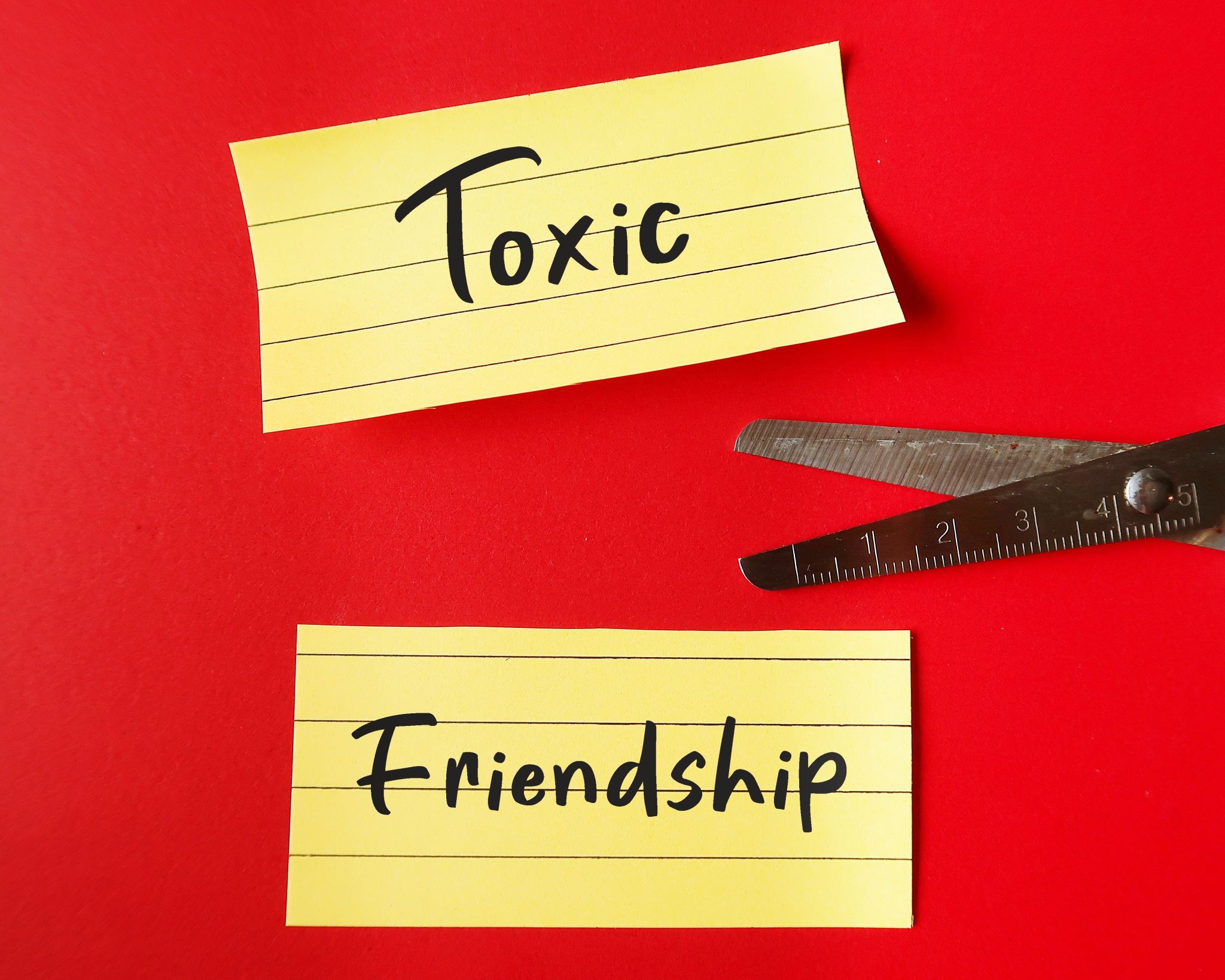 Scissors cutting note paper with handwritten TOXIC FRIENDSHIP, refers to friends who leave negative effects - mentally energy drain and bring down emotionally Scissors cutting note paper with handwritten TOXIC FRIENDSHIP, refers to friends who leave negative effects - mentally energy drain and bring down emotionally