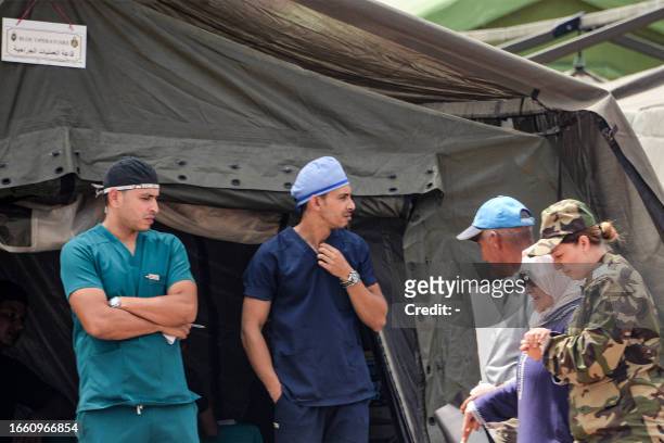 Surgeons stand outside a surgery tent as an elderly woman is assisted to walk by at the military field hospital for earthquake survivors in the...