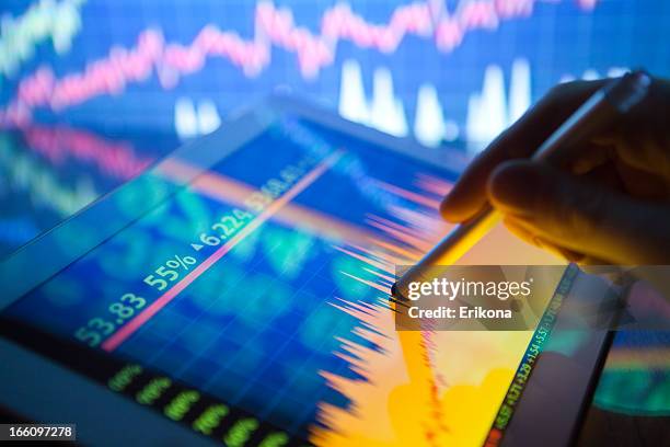 a hand using a digital tablet showing stock fluctuations - global media stock pictures, royalty-free photos & images