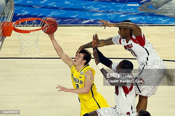 Spike Albrecht of the Michigan Wolverines drives for a shot attempt against Gorgui Dieng and Chane Behanan of the Louisville Cardinals during the...