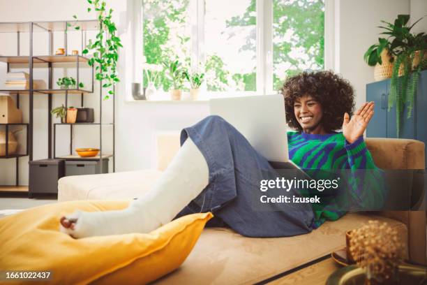 young woman with broken leg using laptop at home - accident recovery stockfoto's en -beelden