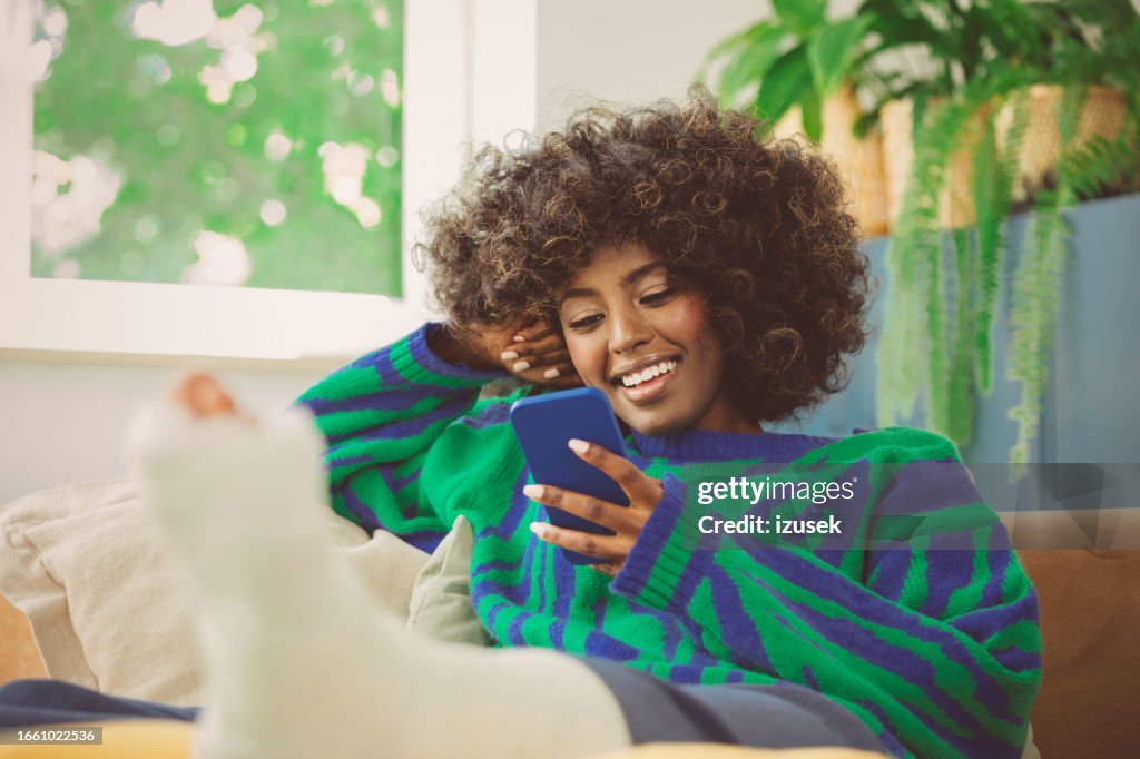 Young woman with broken leg using mobile phone