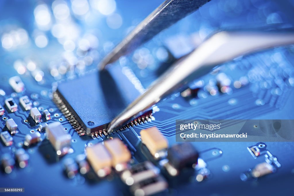 Electronic technician holding tweezers and assemblin a circuit board.