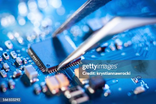 Electronic technician holding tweezers and assemblin a circuit board. Electronic technician holding tweezers and assemblin a circuit board.