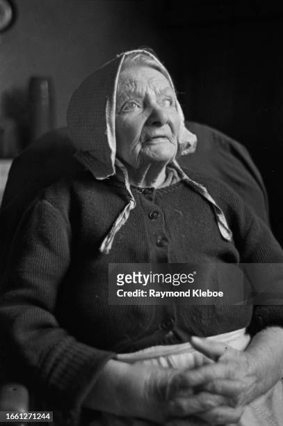 Partially sighted senior woman wearing a bonnet, sits with her hands clasped, Laxton, Nottinghamshire, February 1953. Original Publication: Picture...