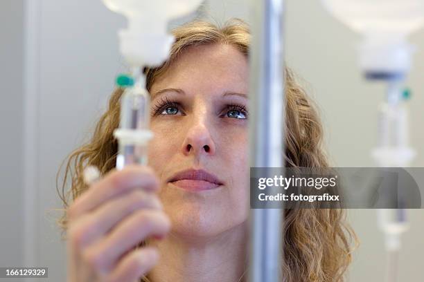 blond female nurse prepares an iv drip - infuus stockfoto's en -beelden