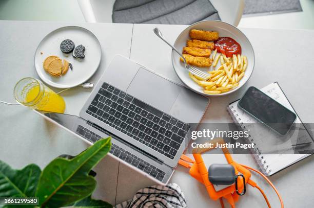 still life of a bowl of fish fingers, chips and tomato ketchup next to where someone is working from home -  an unhealthy working from home lunch - fish finger stock pictures, royalty-free photos & images