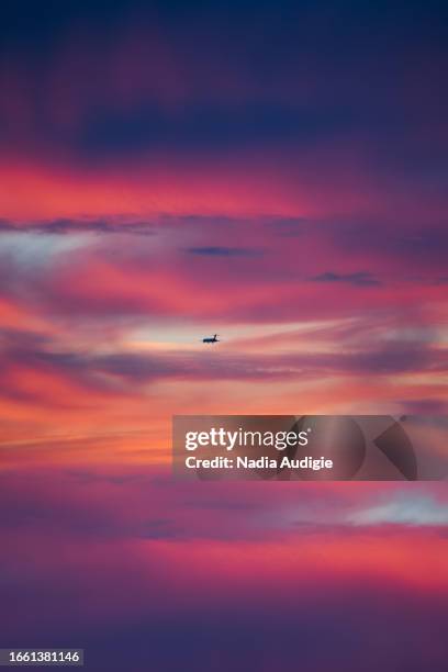 dramatic clouds on a sunset sunrise sky with orange blue purple and pink etherial pastel background with flying plane - plane purple sky stock pictures, royalty-free photos & images