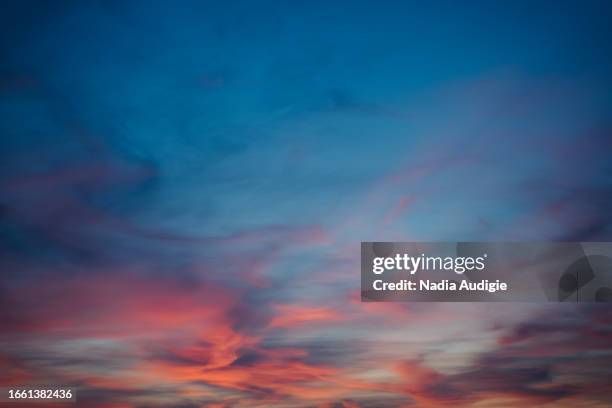 dramatic clouds on a sunset sunrise sky with orange blue purple and pink etherial pastel background - solnedgång bildbanksfoton och bilder