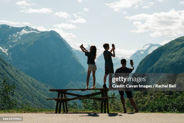 family taking pictures with their phones of a beautiful view in norway - summer super 8 stockfoto's en -beelden