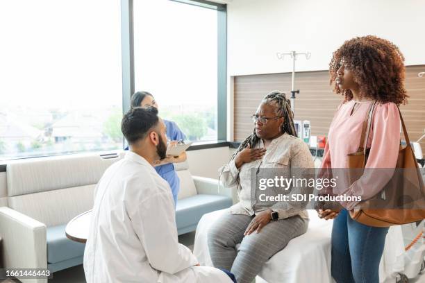 woman gestures to self while talking to er doctor - spoedeisende geneeskunde stockfoto's en -beelden