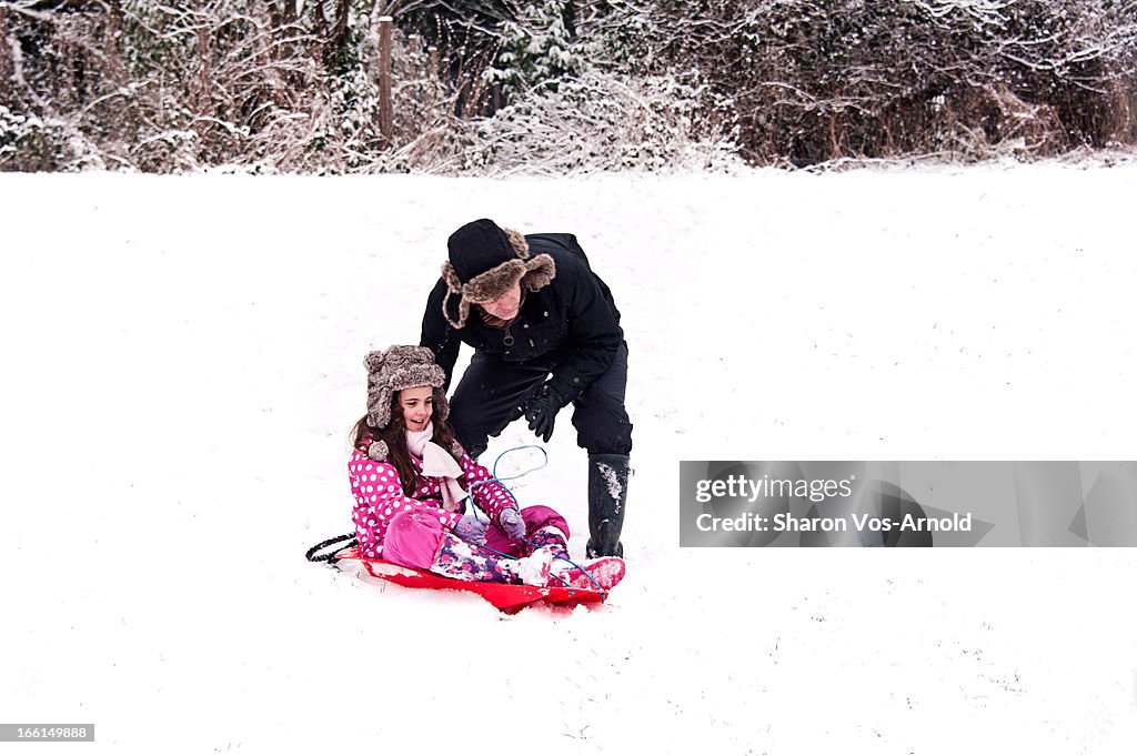 Dad pushing girl on a red sledge in snow