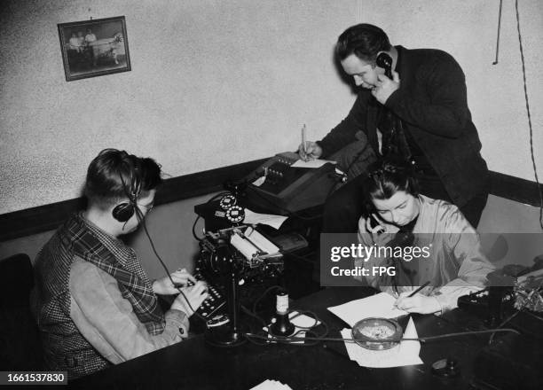 Person wearing a hands-free headset as they sit at a typewriter as two other people hold telephone receivers as they respond to callers during the...