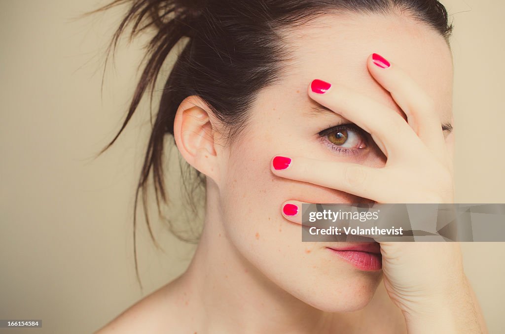 Misterious girl with red nails and hand on face.