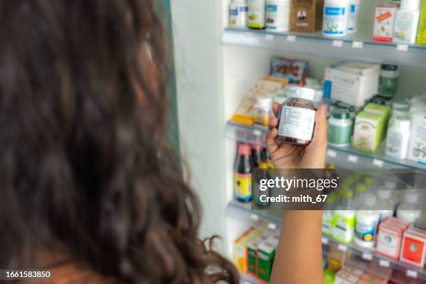 client latin non reconnu dans la pharmacie tenant un flacon de médicament, lisant le texte de l’étiquette sur les informations médicales ou les effets secondaires dans la pharmacie. pilules d’achat de patients pour la migraine ou la grippe. - étiqueter photos et images de collection