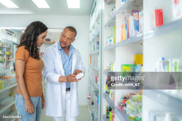 latin mid adult female customer listening, talking to professional black pharmacist male at drug store. mid adult african american pharmacist male with skinhead and beard
explaining medication following the instruction from label to customer. - allergy medicine stock pictures, royalty-free photos & images