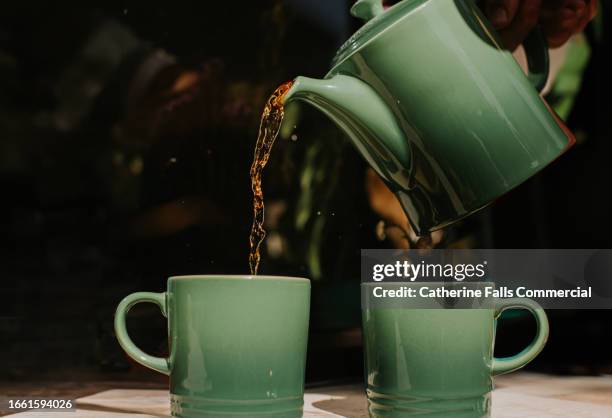 tea is poured from a green teapot into matching mugs - tea fotografías e imágenes de stock