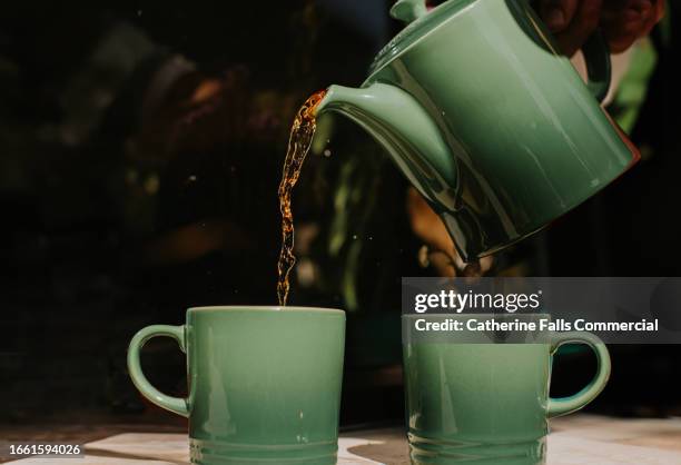 tea is poured from a green teapot into matching mugs - hojas de té secas fotografías e imágenes de stock