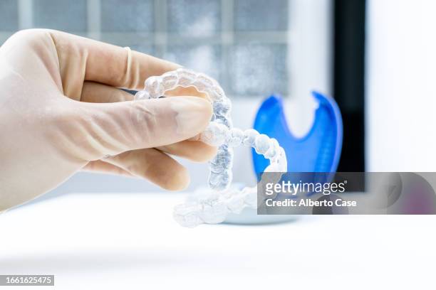 an unrecognizable orthodontist holding two clear dental aligners in a dental clinic - human mouth stock photos et images de collection