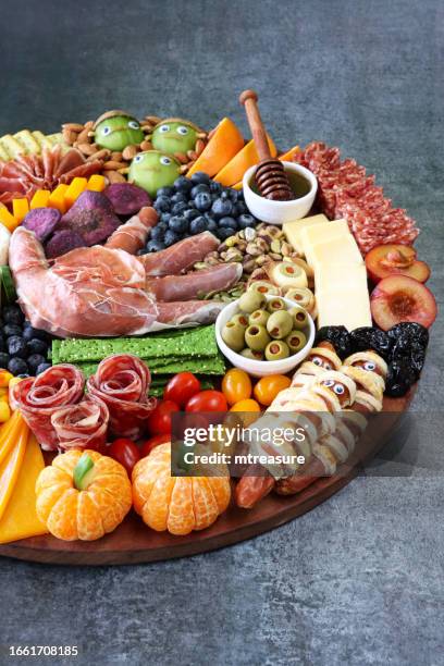 image of cheese-charcuterie board, prosciutto di parma hand, pink grapefruit, salami roses, cheddar cubes, cherry tomatoes, frankenstein monster kiwi fruit, almonds, sausage mummies, blueberries, satsuma pumpkins, grey background, focus on foreground - frankenstein stock pictures, royalty-free photos & images