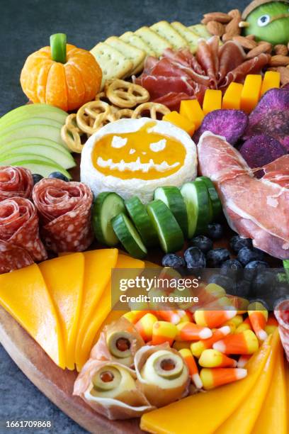 close-up image of cheese-charcuterie board, prosciutto di parma hand, pumpkin brie, salami roses, cheddar cubes, cherry tomatoes, frankenstein monster kiwi fruit, almonds, sausage mummies, blueberries, satsuma pumpkin, grey background, focus on foreground - frankenstein stock pictures, royalty-free photos & images