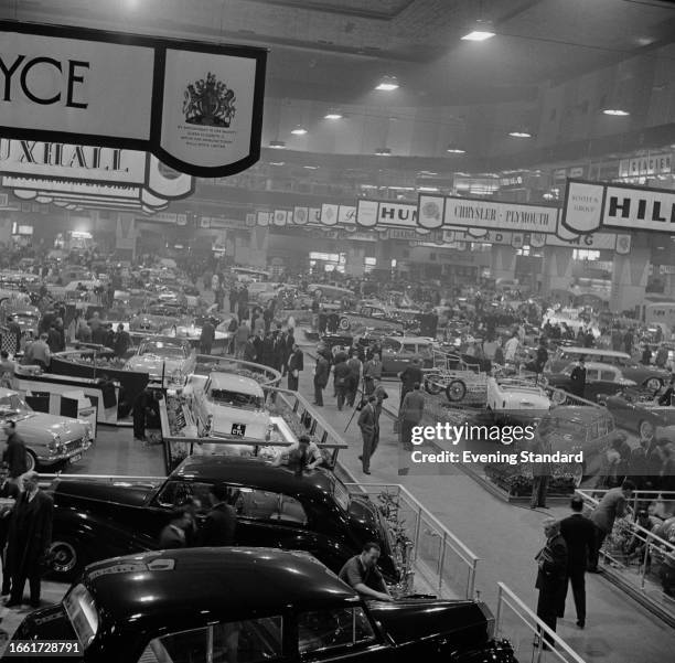 Visitors walking among exhibition stands showing new cars, signposted with various car brands at the London Motor Show, Earl's Court, October 1957.