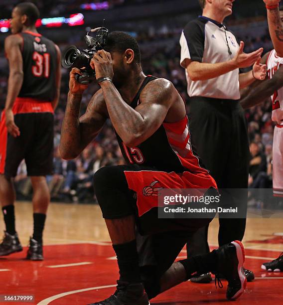 Amir Johnson of the Toronto Raptors pretends to take a picture with a remote camera that was kicked onto the floor during a game against the Chicago...