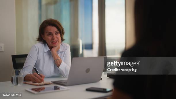 female mental health professional listening and giving advice to her patient - 50s woman writing at table imagens e fotografias de stock
