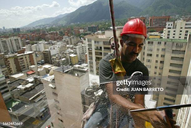 Un obrero limpia vidrios en una torre al este de Caracas el 14 de julio de 2003. El Impuesto al Débito Bancario bajo de 1 a 0,75 % al tiempo que el...