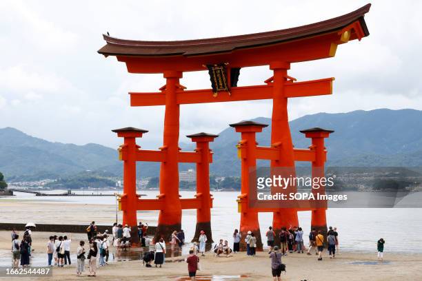 Tourists pose in front of a giant "torii" gateway at Itsukushima Shrine on Miyajima Island in Hatsukaichi, Hiroshima Prefecture. Itsukushima Shrine,...
