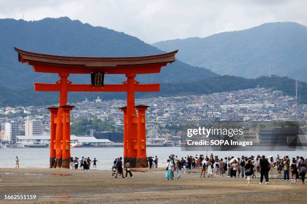 Tourists pose in front of a giant "torii" gateway at Itsukushima Shrine on Miyajima Island in Hatsukaichi in Hiroshima Prefecture. Itsukushima...