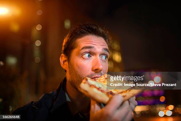 man eating pizza on city street - american pizza stock-fotos und bilder