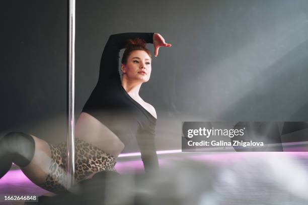 young red haired woman in sportswear dancing on pole in the studio - pole dancing class stock pictures, royalty-free photos & images