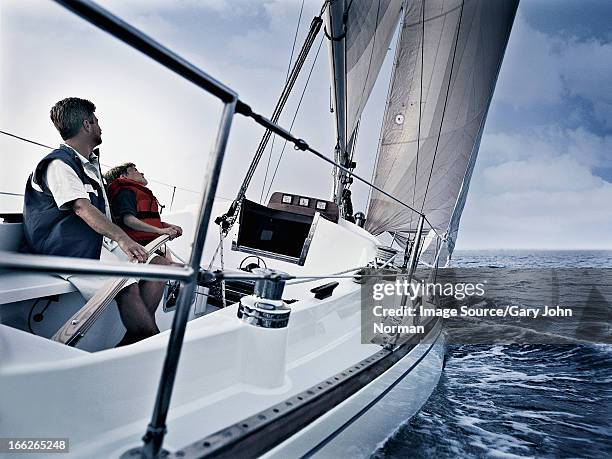 father and son steering boat on water - kid sailing stock-fotos und bilder