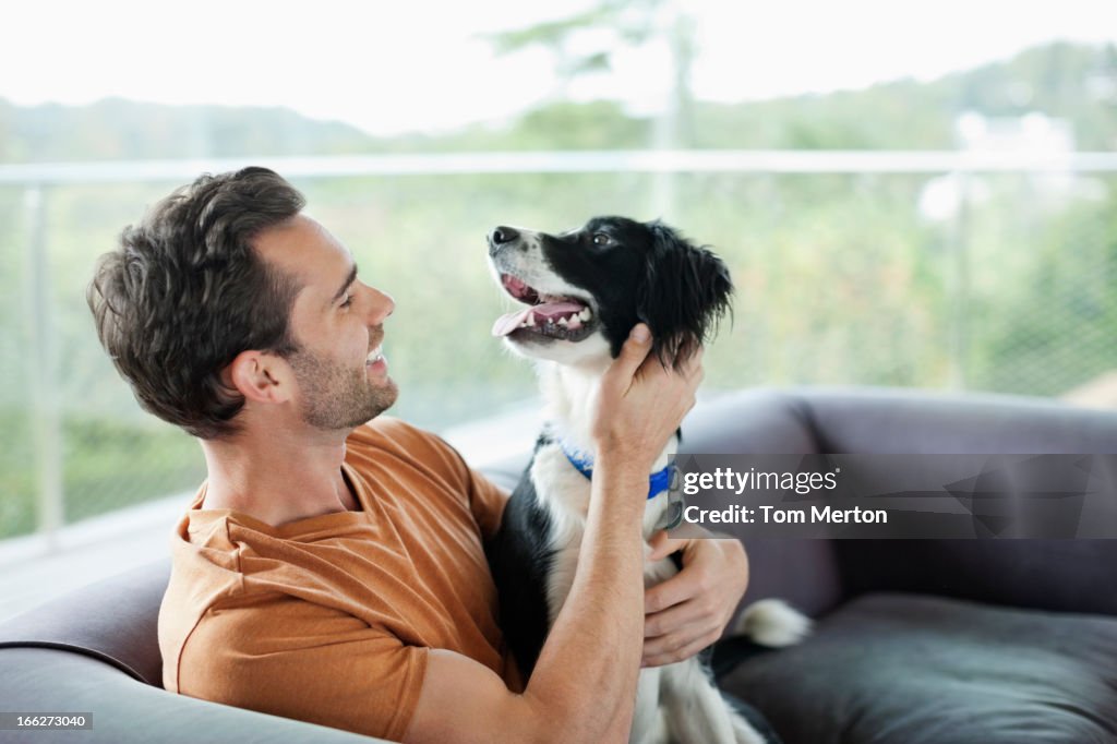Smiling man petting dog on sofa