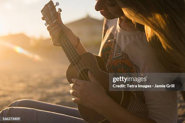 usa, new york state, rockaway beach, woman playing ukulele at sunset - ukulele foto e immagini stock