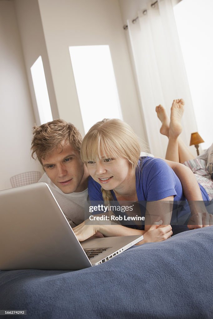 Couple lying on bed using laptop