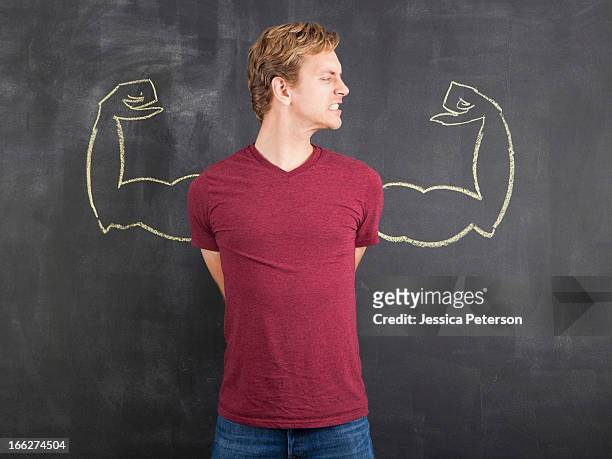 studio shot of mid adult man with hands behind back and chalk drawing of artificial arms on blackboard - wit blackboard stock-fotos und bilder