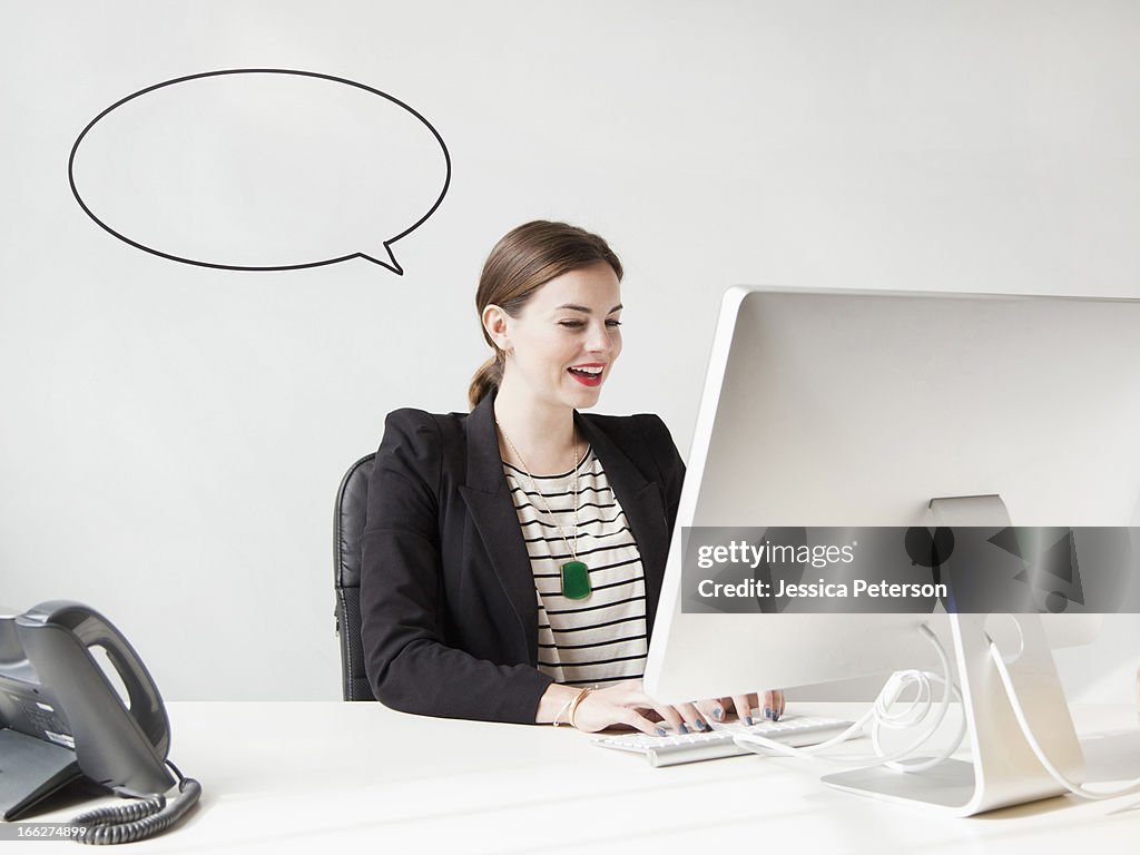 Studio shot of young woman working on computer with speech bubble next to her head