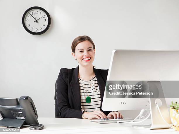 studio shot portrait of young woman working on computer and smiling - clock person desk stockfoto's en -beelden