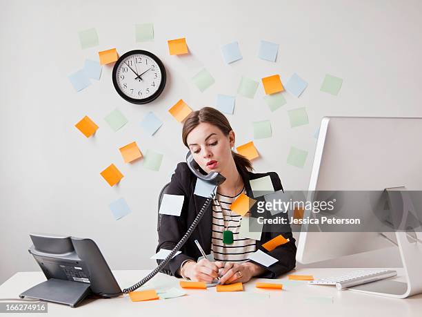 studio shot of young woman working in office covered with adhesive notes - clock person desk stockfoto's en -beelden