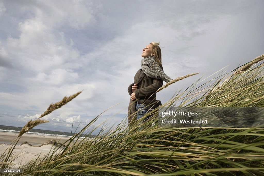 Germany, Schleswig Holstein, Amrum, Young woman on grassy sand dune