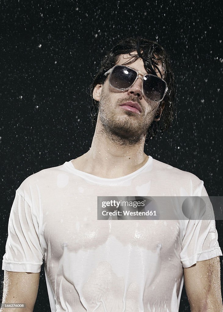 Man standing in rain, wearing sunglasses.