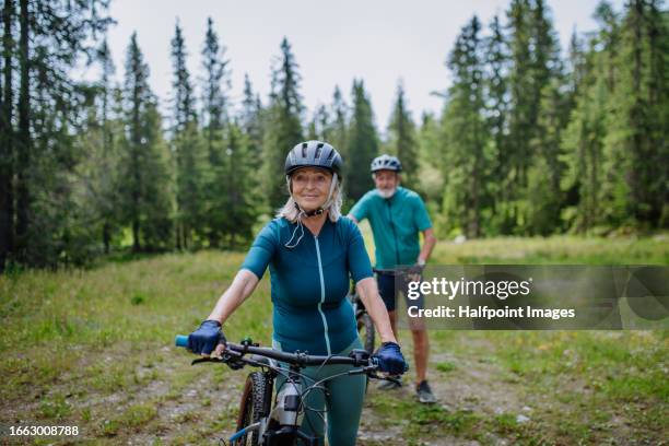 portrait of senior woman cyclist resting, pushing bike along a forest trail. - fahrrad fahren alte leute beine stock-fotos und bilder
