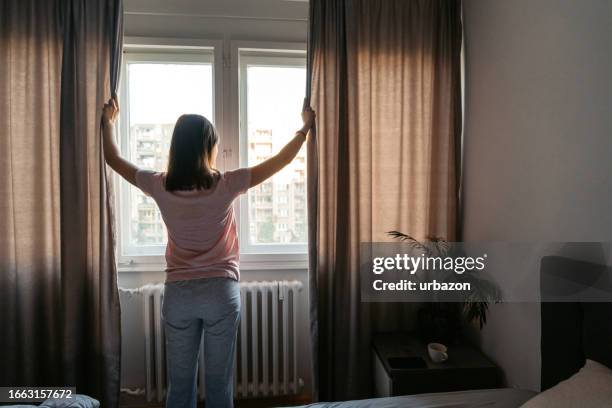young woman opening up curtains in the bedroom in the morning - overslept stock pictures, royalty-free photos & images